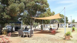 Un patio al aire libre con mesas y sillas, rodeado de árboles y un edificio al fondo.
