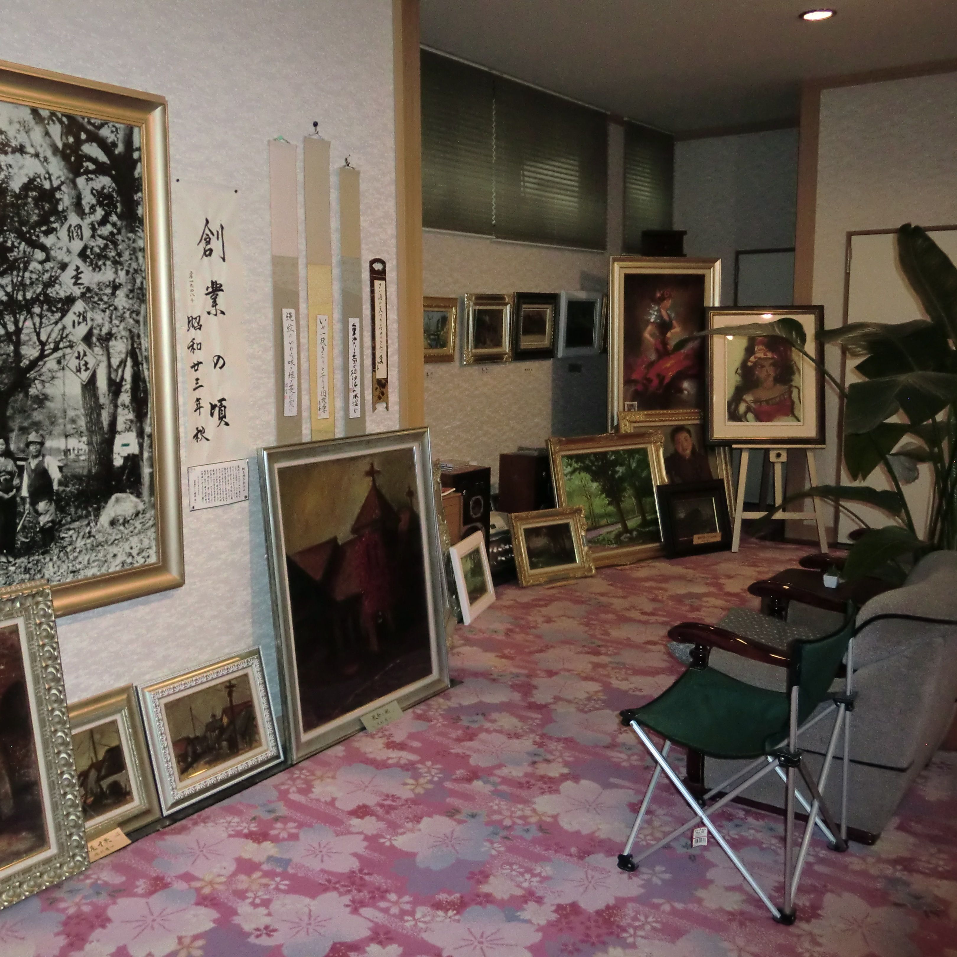 A room with multiple framed artworks on the walls, a green folding chair, and a patterned carpet.