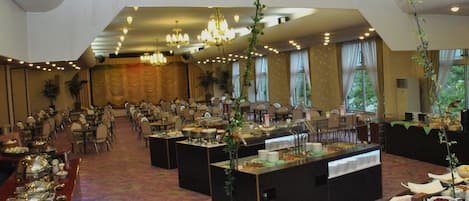 Un salón de banquetes con varias mesas, una zona de buffet y plantas colgantes.