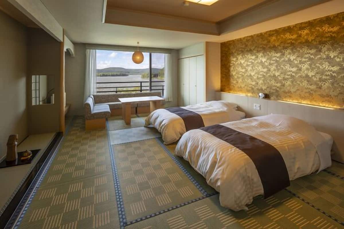 Una habitación con dos camas, vistas al exterior, una mesa y un banco.