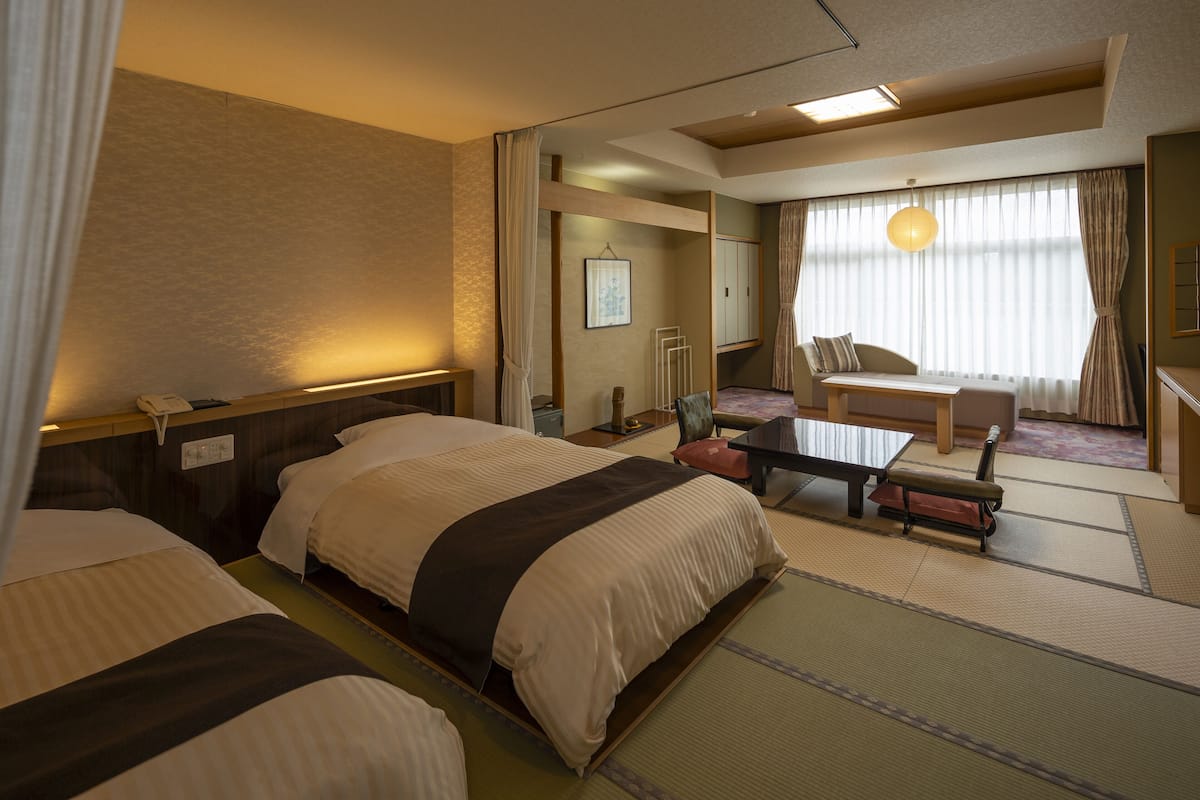 Une chambre d’hôtel avec deux lits, un bureau, une chaise et une grande fenêtre avec des rideaux.