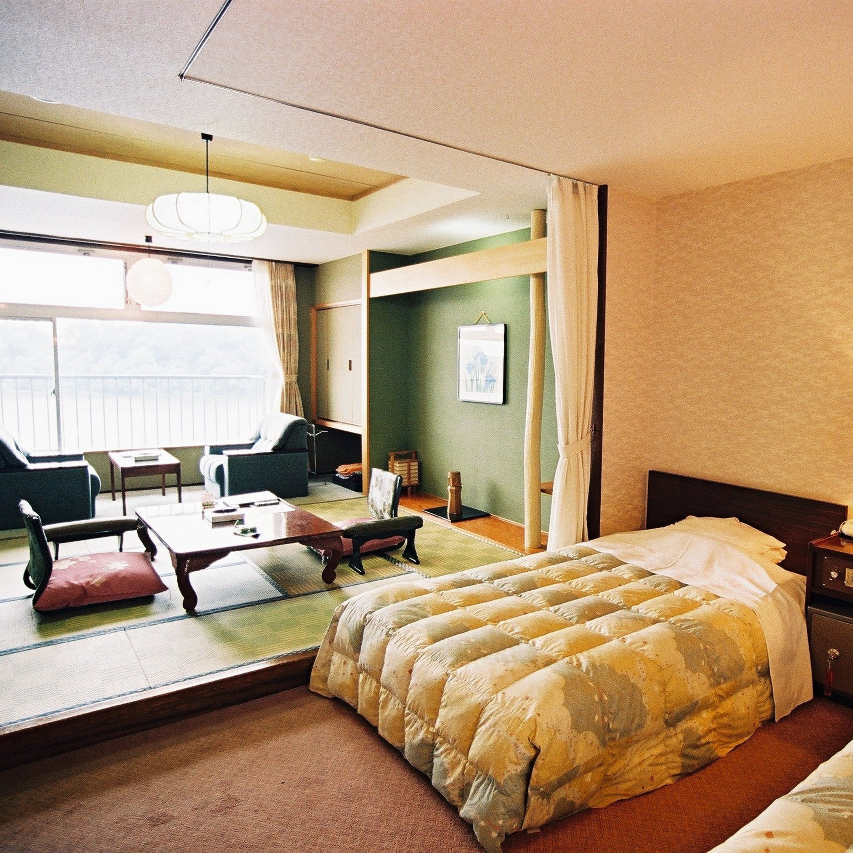 A hotel room with a bed, a seating area with a table and chairs, a large mirror, and a view of the outdoors.