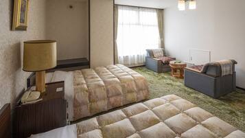 A hotel room with two beds, a desk with a lamp, a chair, a small table, and a window with curtains.