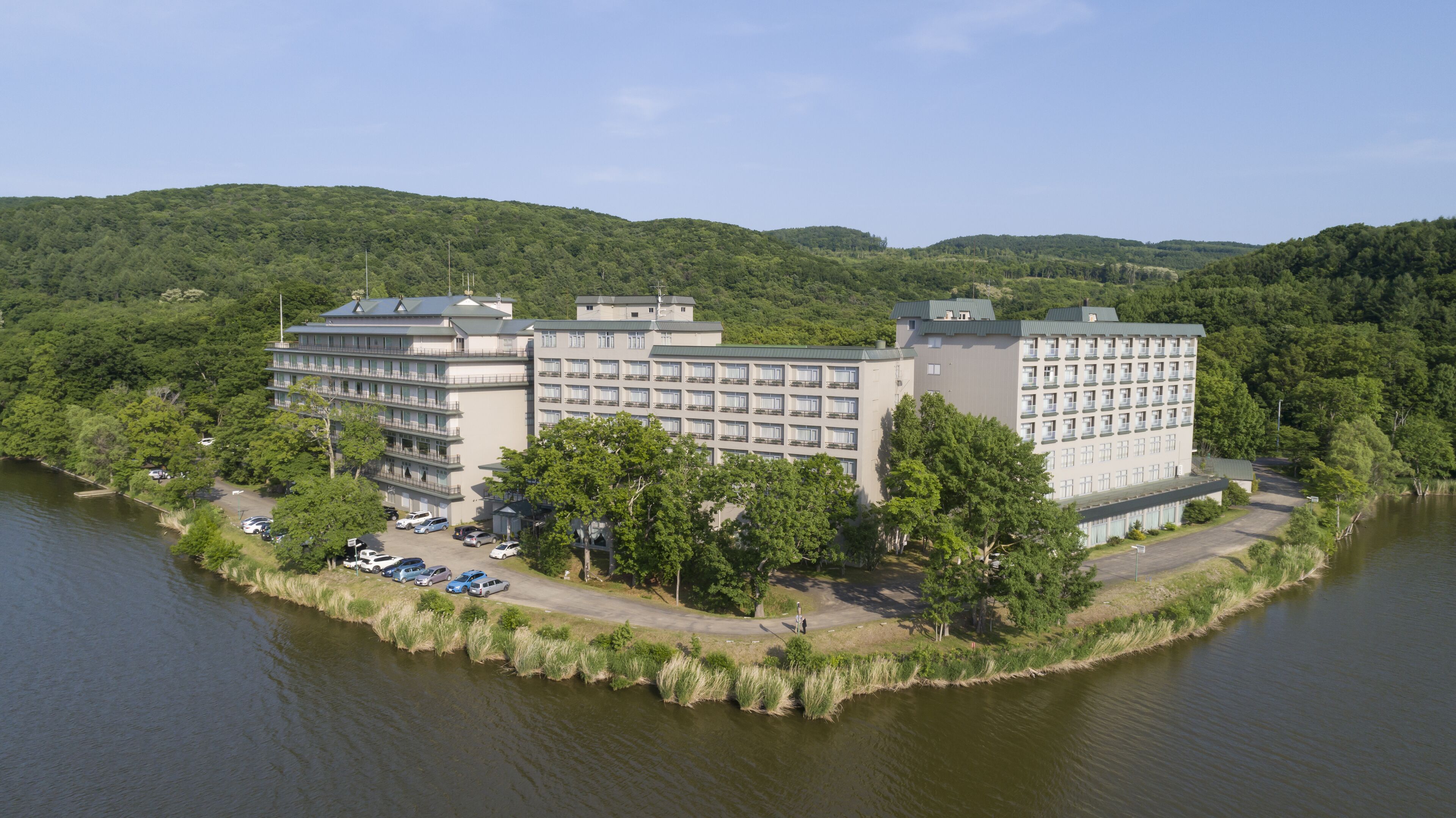 A large hotel with multiple floors and balconies, situated by a lake with a parking area in front.