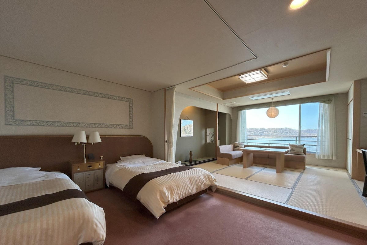 Une chambre d’hôtel avec deux lits, un coin salon avec vue et une grande fenêtre.