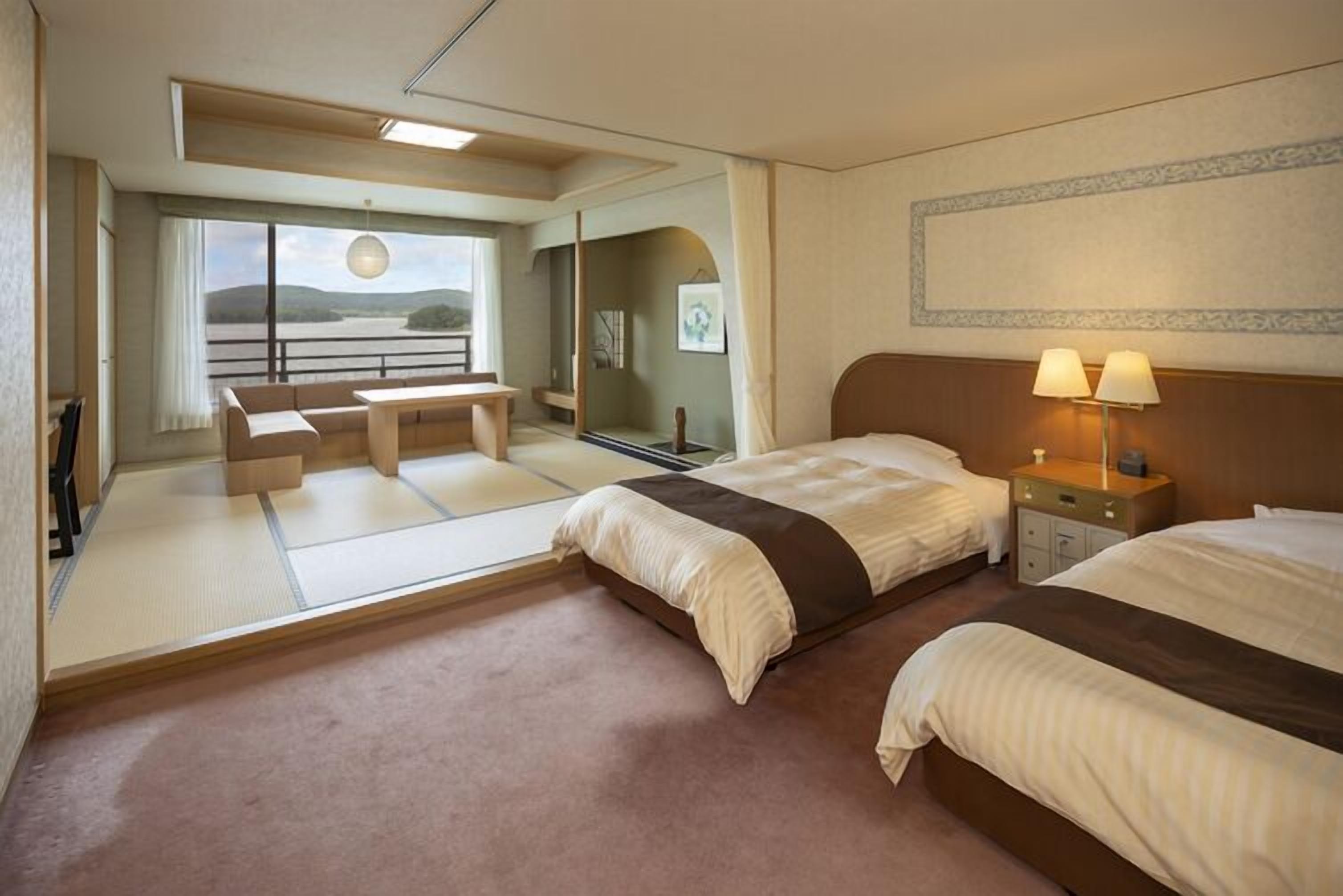 Une chambre d’hôtel avec deux lits, un bureau, une chaise, un canapé, une vue sur l’extérieur et une lampe sur la table de chevet.