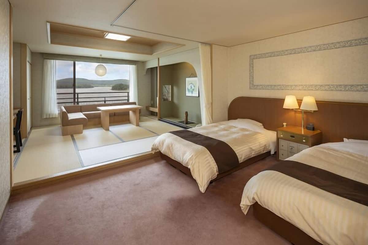 Une chambre d’hôtel avec deux lits, un bureau, une chaise, un canapé, une vue sur l’extérieur et une lampe sur la table de chevet.
