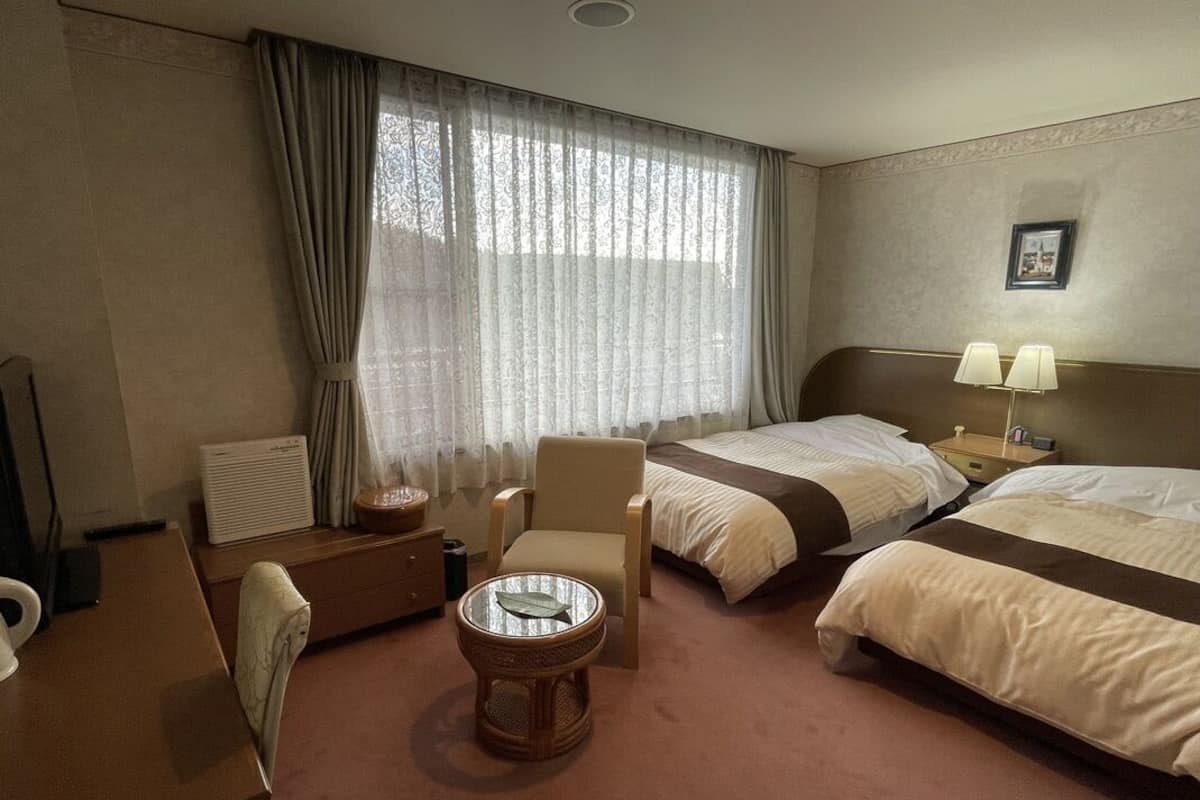 Une chambre d’hôtel avec deux lits, un bureau, une chaise, une petite table ronde et une fenêtre avec des rideaux.