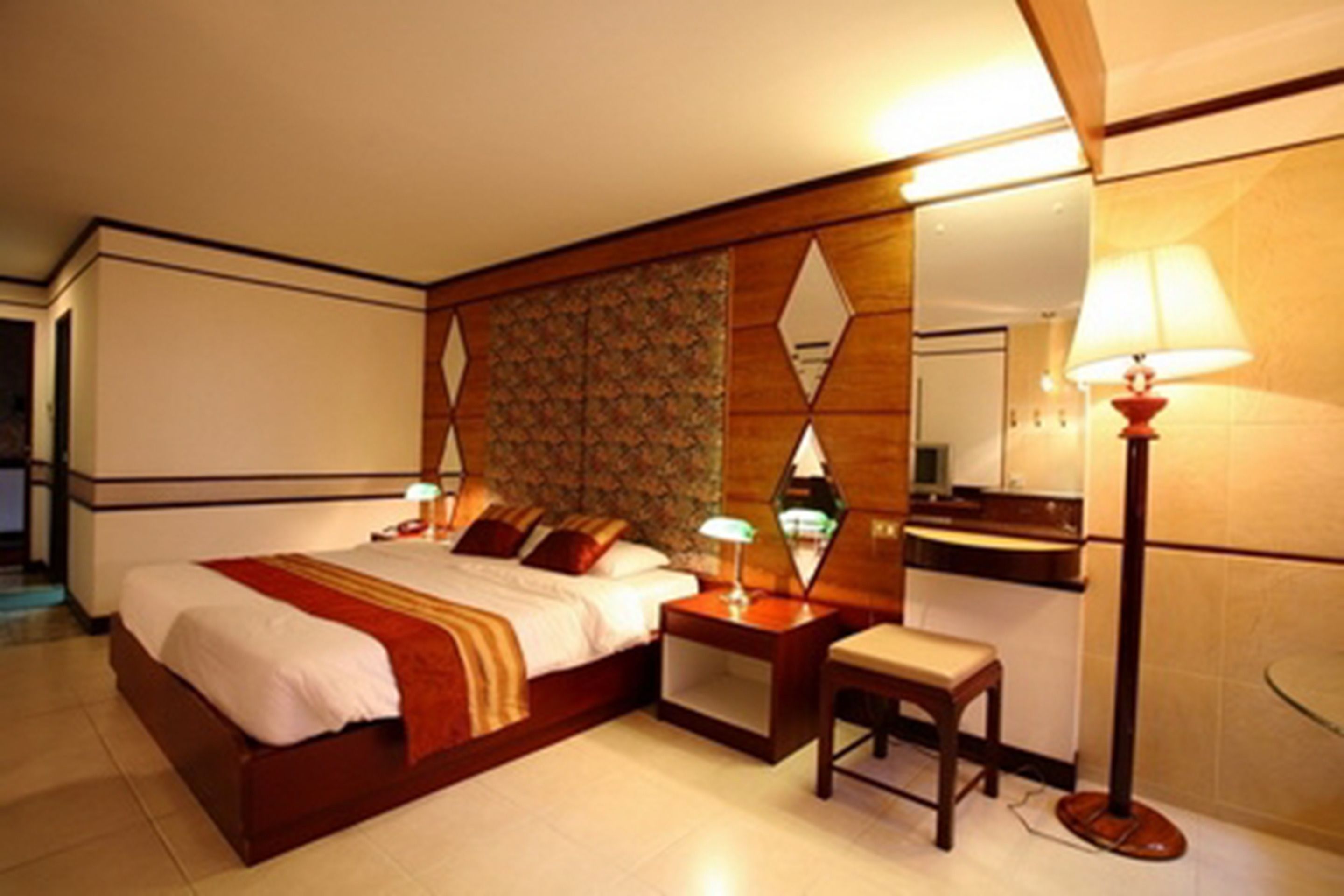 A hotel room with a large bed, a bedside table with a lamp, a small stool, and a mirror.