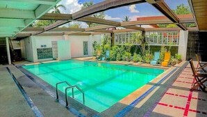 A swimming pool with a tiled deck, surrounded by potted plants and a covered area with chairs. - The Pacific Cool Chic (Chiang Mai)