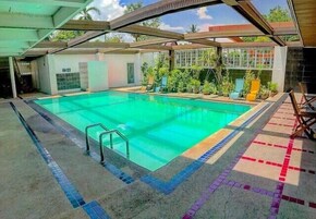 A swimming pool with a tiled deck, surrounded by potted plants and a covered area with chairs.