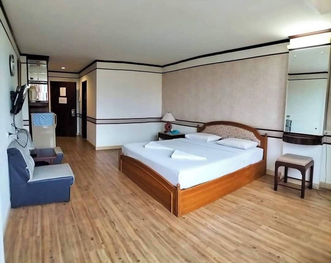 A hotel room with a wooden floor, a bed with white linens, a bedside table, a lamp, and a small stool.