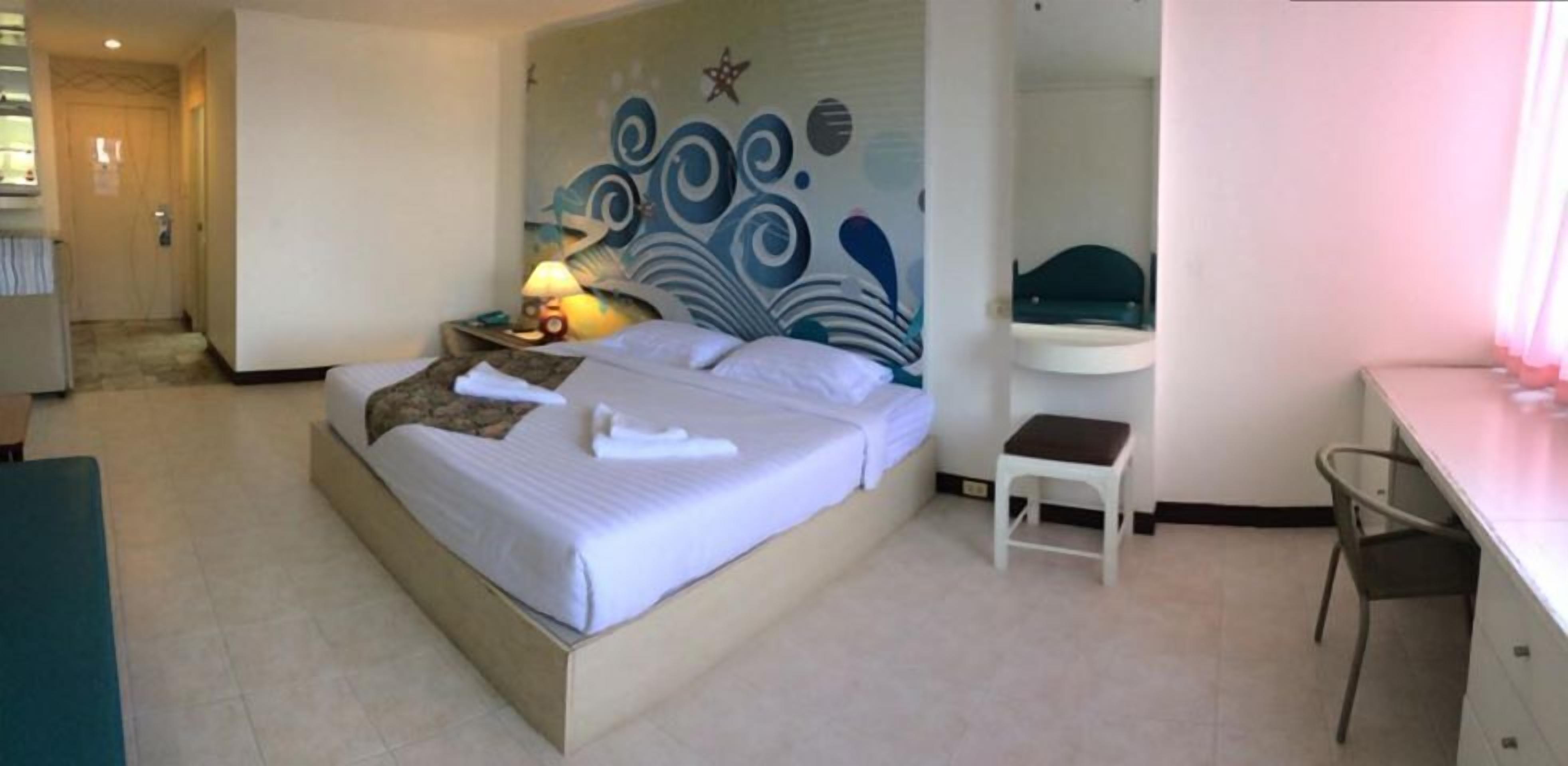 Una habitación de hotel con cama, escritorio, silla, mesita de noche y decoración en la pared.