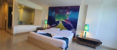 Habitación de hotel con una cama grande, dos mesitas de noche con lámparas, un espejo amplio y un mural colorido en la pared.