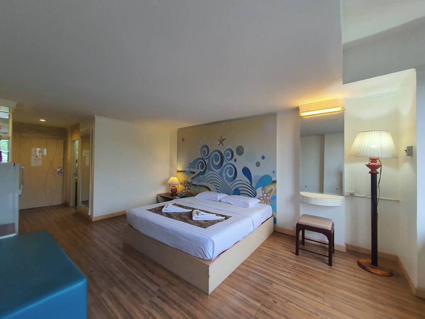 A hotel room with a bed, bedside table, lamp, and a wall mural.
