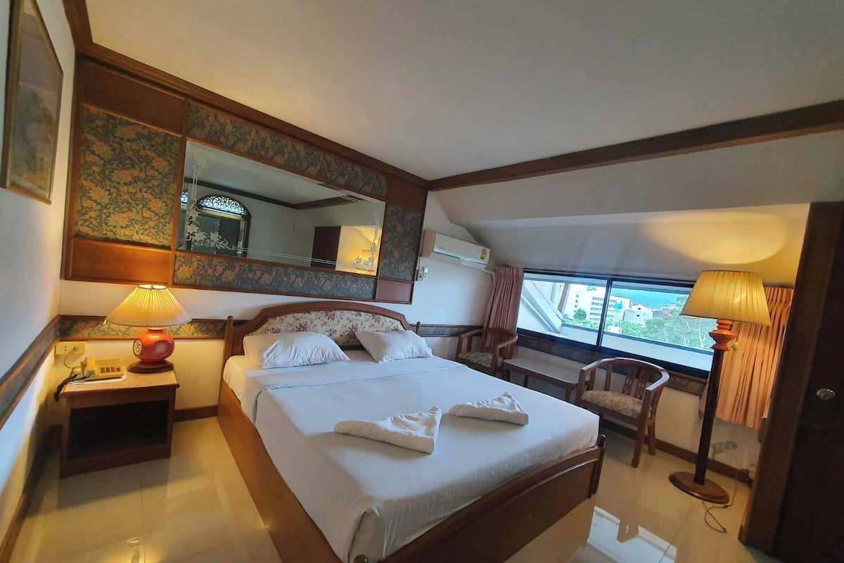 Ein Hotelzimmer mit einem großen Bett, einem Schreibtisch mit Lampe, einem Stuhl, einem Fenster mit Blick und einem Spiegel.