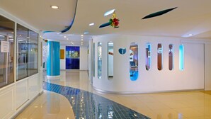 A modern hotel lobby with a curved reception desk, glass doors, and a blue-tiled floor. - The Pacific Cool Chic (Chiang Mai)