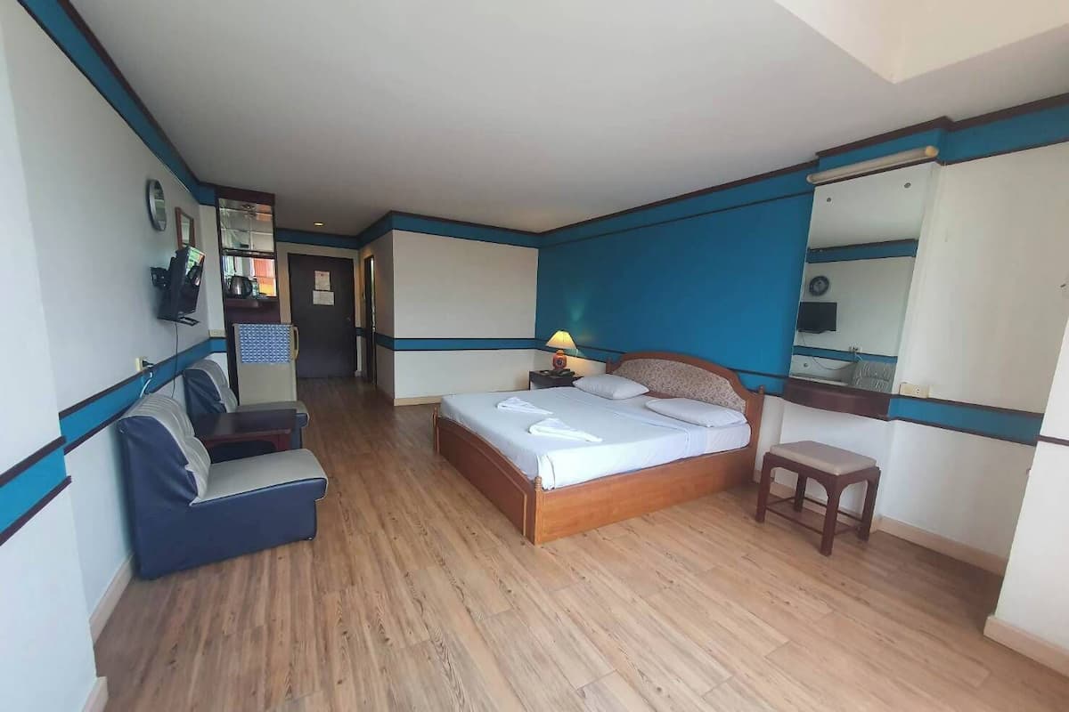 Ein Hotelzimmer mit einem Bett, einem Schreibtisch, einem Sessel, einem Spiegel und Holzboden.