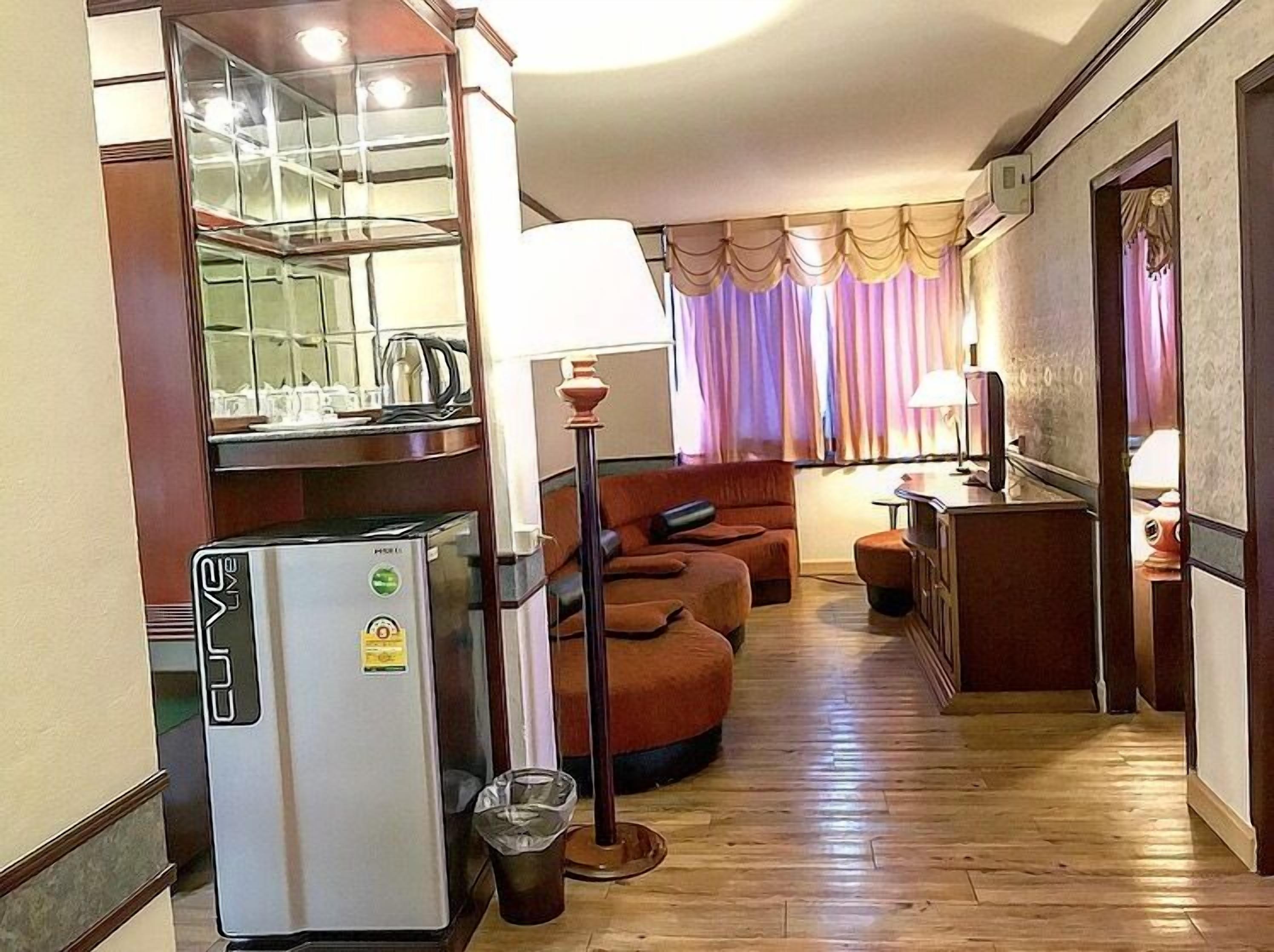 Kompakti hotellihuone, jossa on pieni keittiönurkkaus, sohva, pieni pöytä ja lamppu.