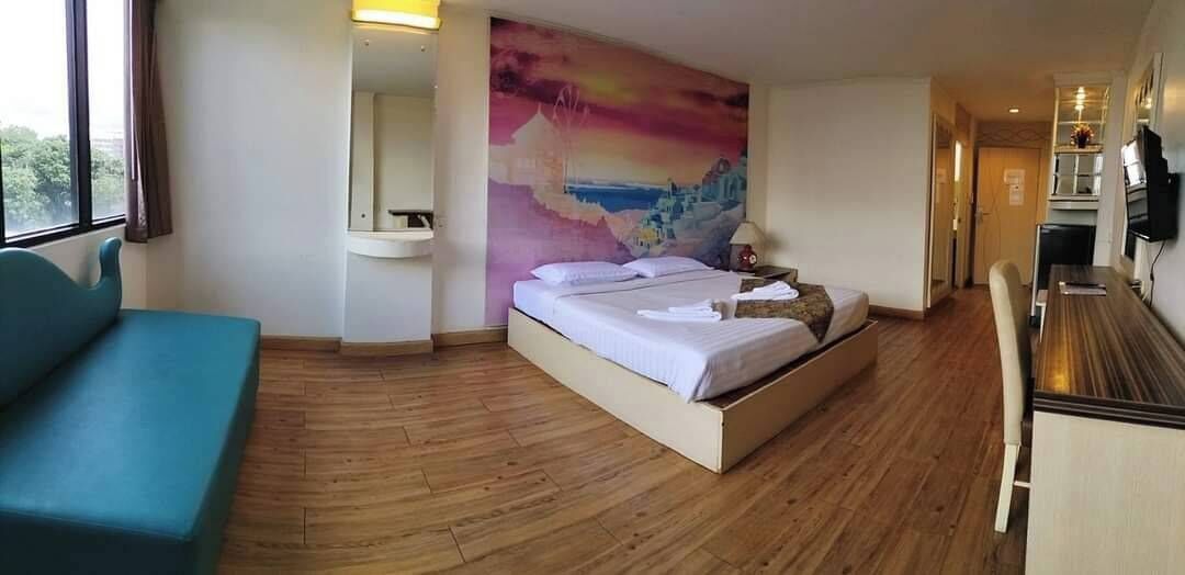 Una habitación de hotel con una cama, un sofá azul, un cuadro en la pared, una mesita con una lámpara y un televisor en la pared.