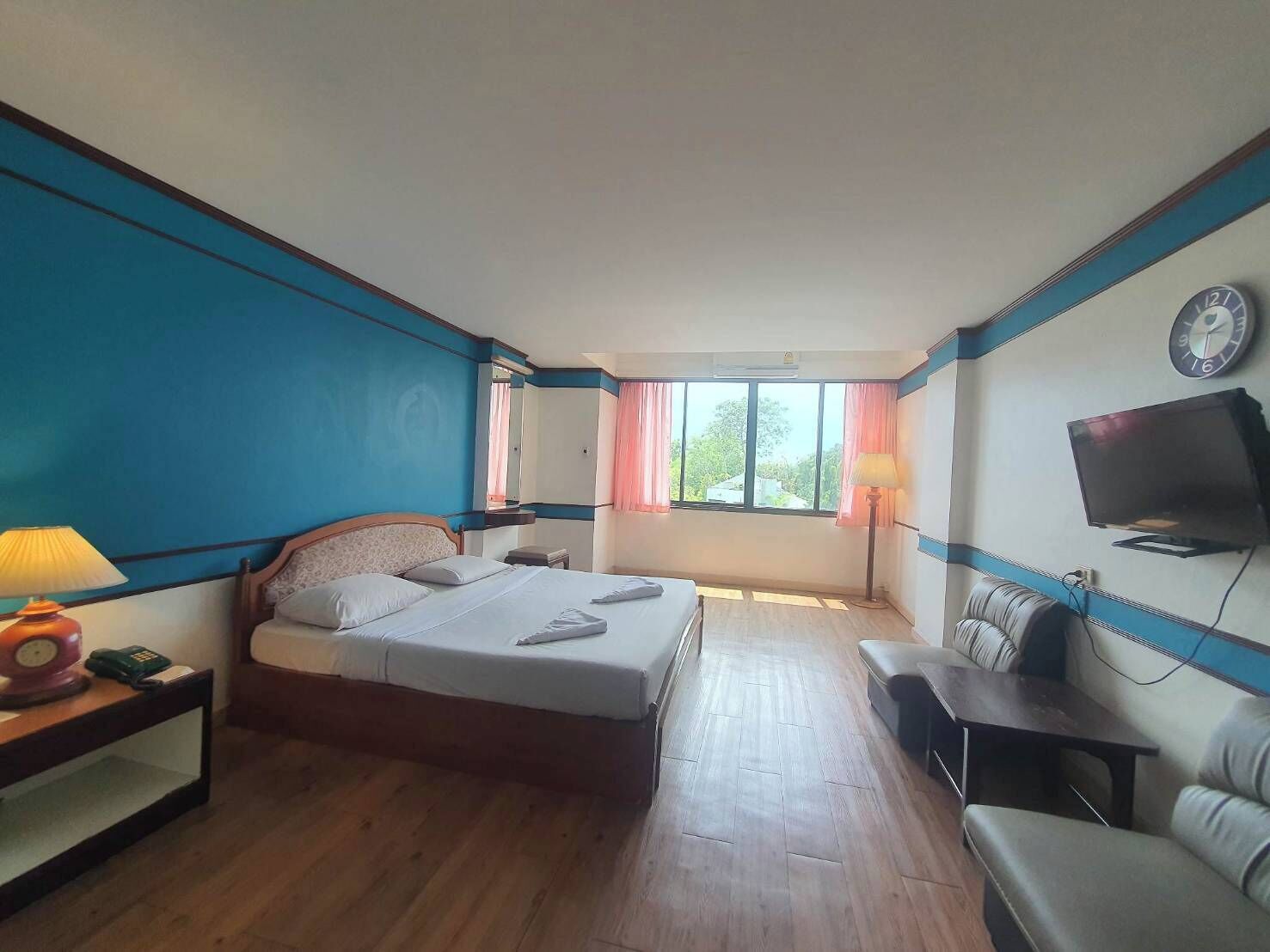 Een hotelkamer met een bed, nachtkastje, lamp, televisie en een bank.