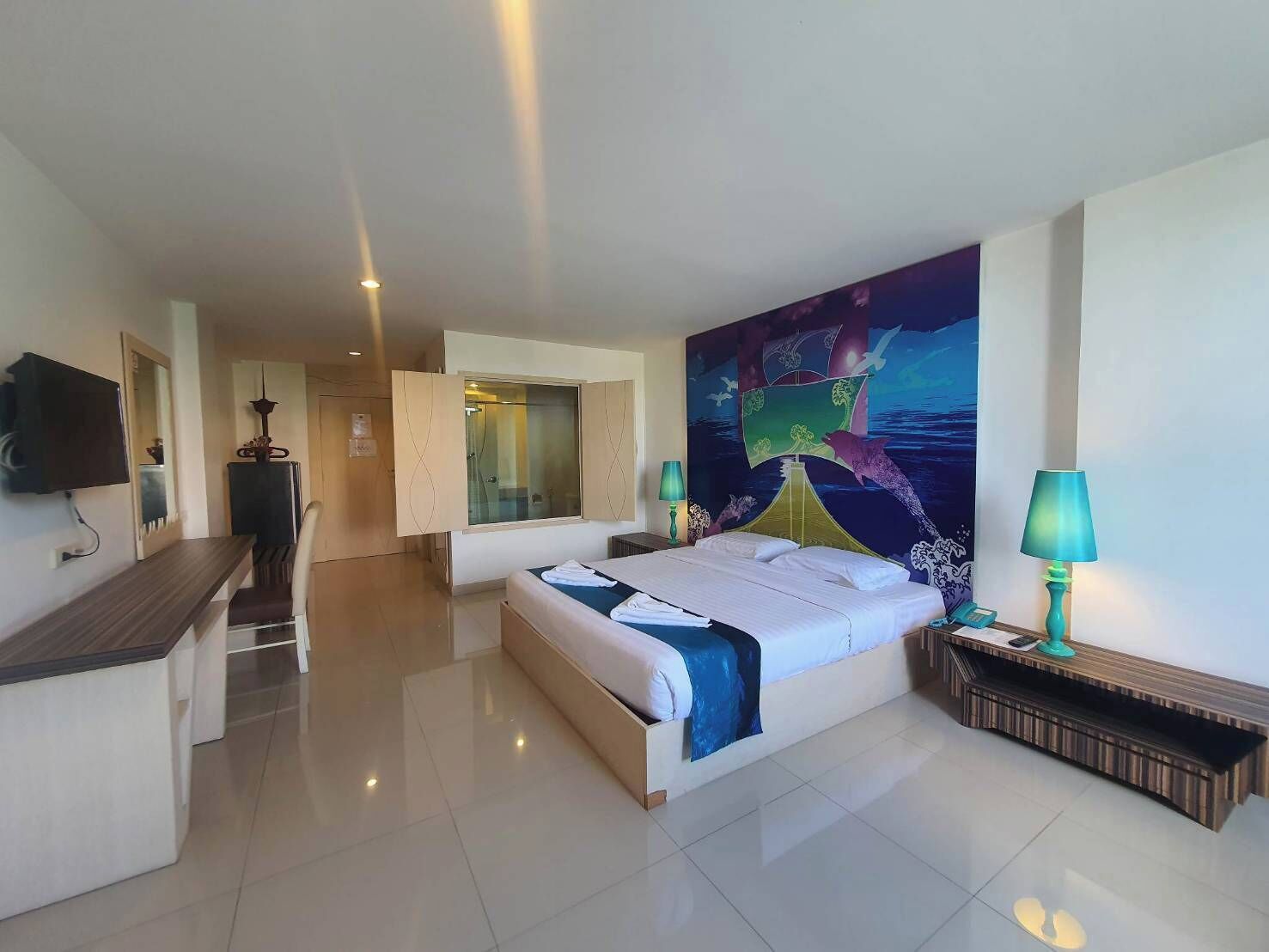 A modern hotel room with a large bed, a desk, a television, and a bathroom with a glass shower enclosure.