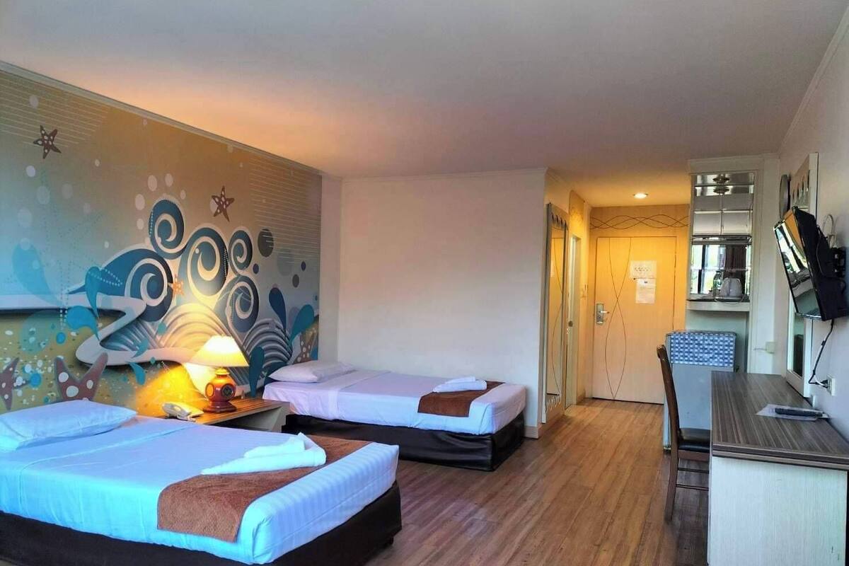 Ein Hotelzimmer mit zwei Betten, einem Schreibtisch, einer Küchenzeile und einer Wand mit abstrakter Kunst.