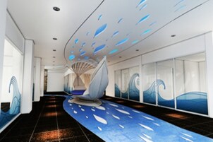 A modern hotel lobby with a curved ceiling, wave-themed wall art, and a central seating area.