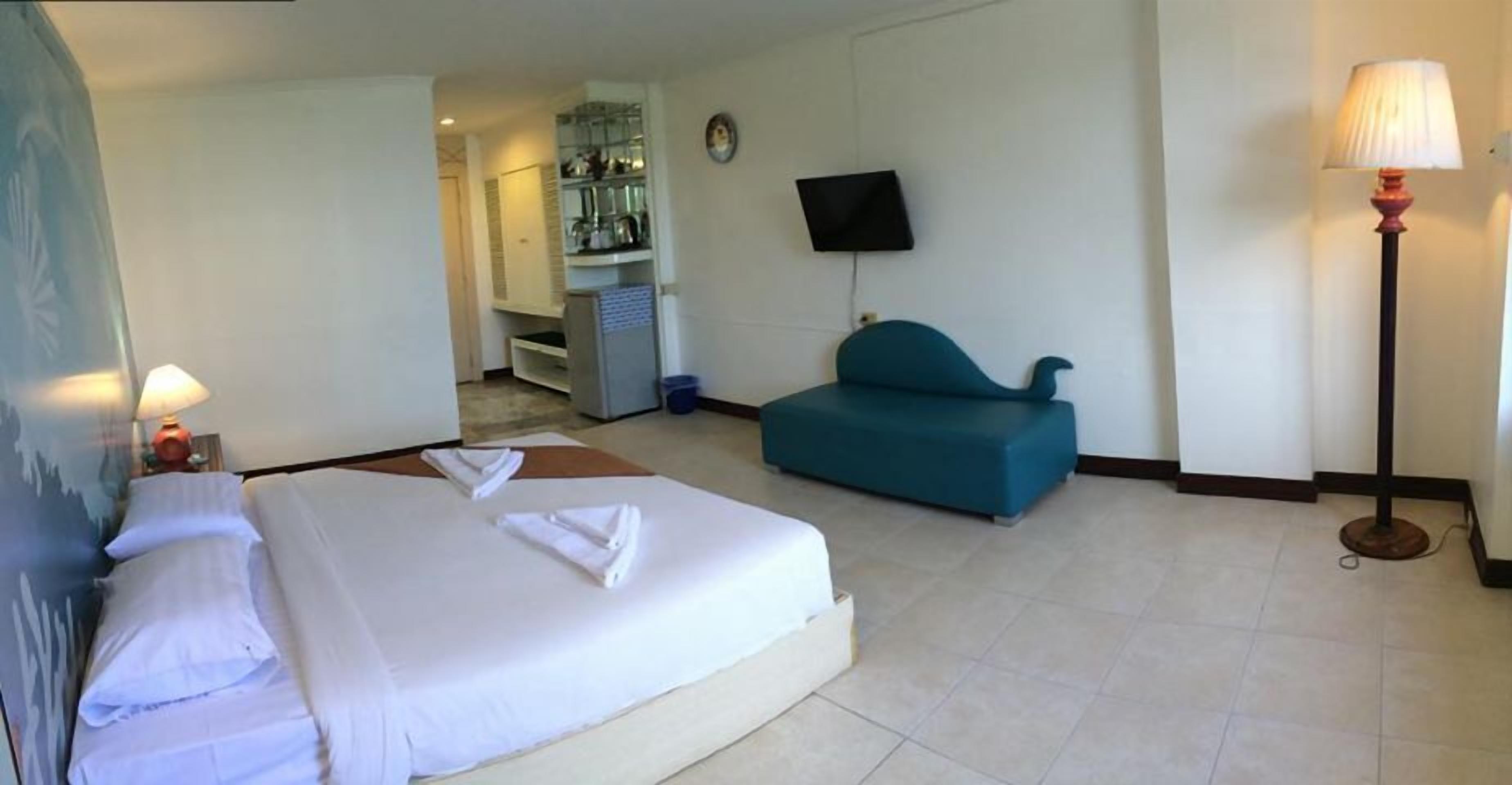 A hotel room with a bed, a sofa, a TV, and a lamp.