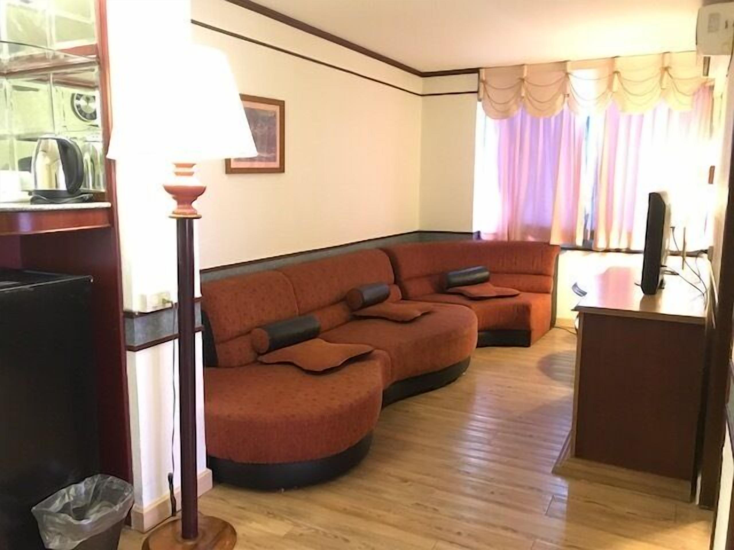 Ein Wohnzimmer mit einem Ecksofa, einem kleinen Schreibtisch, einer Lampe und einem Papierkorb.