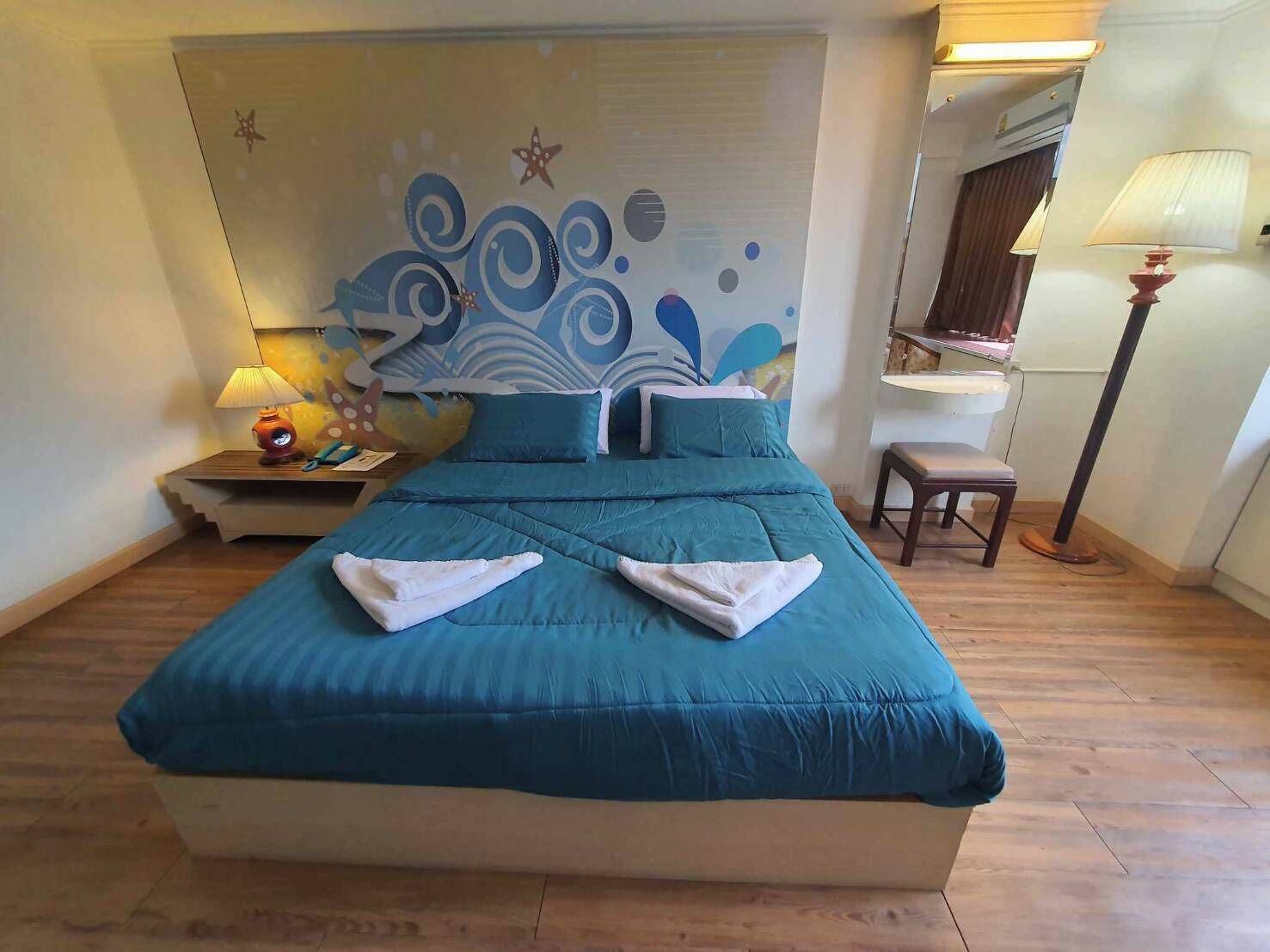 A neatly made bed with a blue bedspread and pillows, a bedside table with a lamp, and a chair.