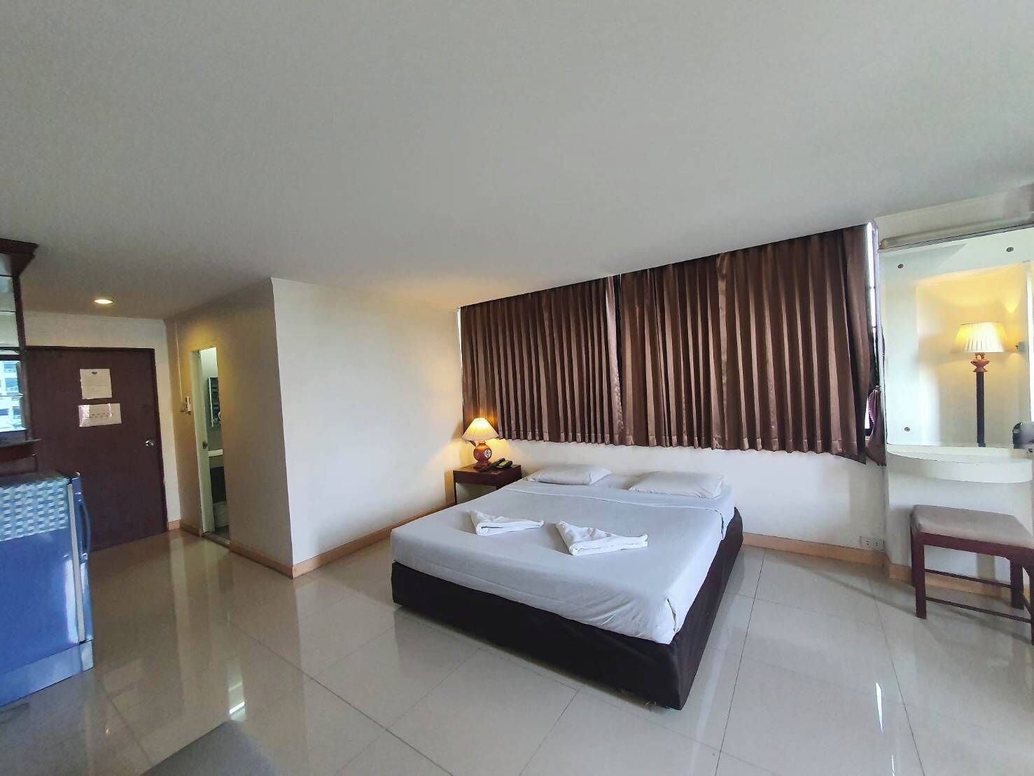 A hotel room with a large bed, a bedside table with a lamp, a mirror, and a small seating area.