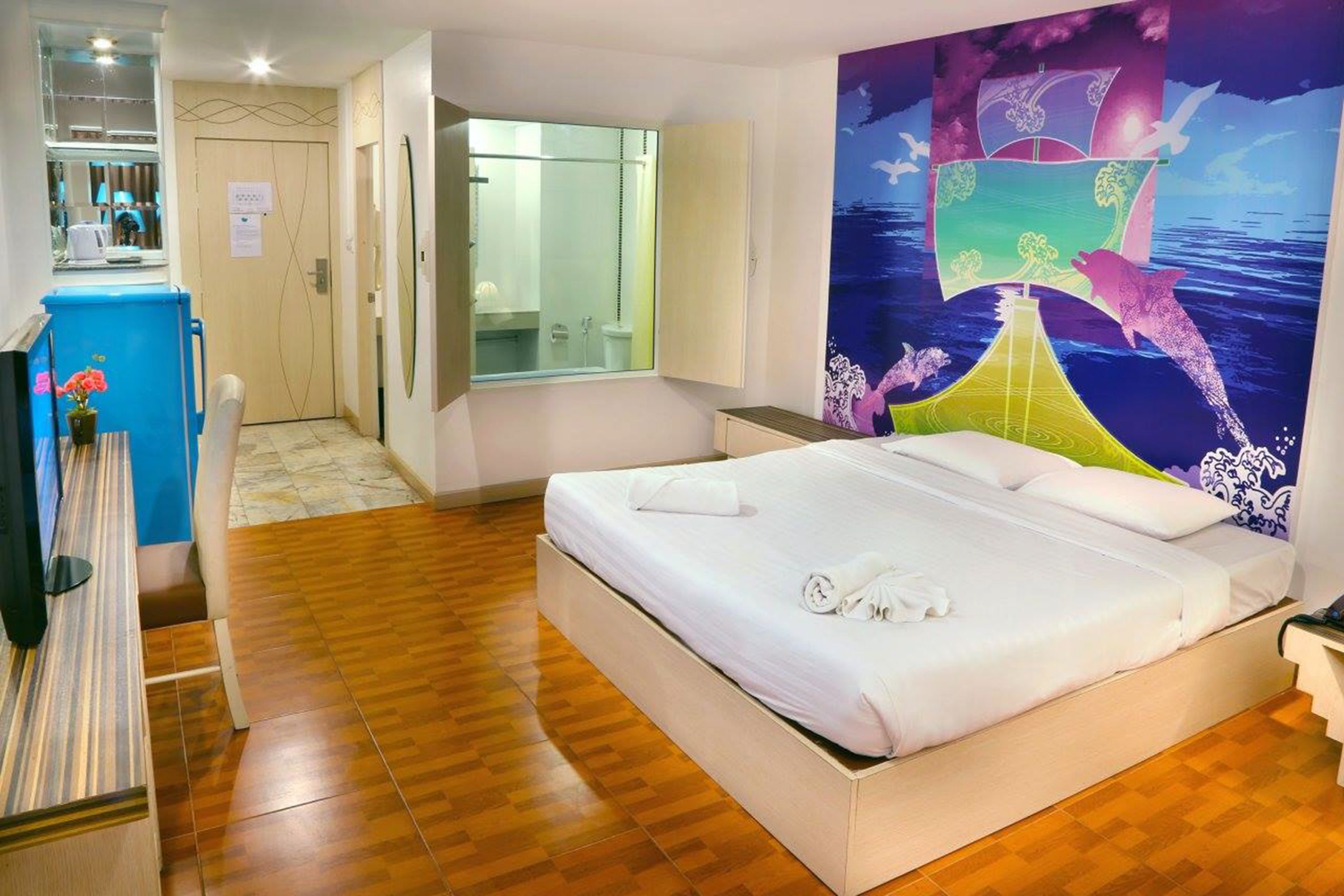 A hotel room with a large bed, a bathroom with a glass shower, and a colorful mural on the wall.
