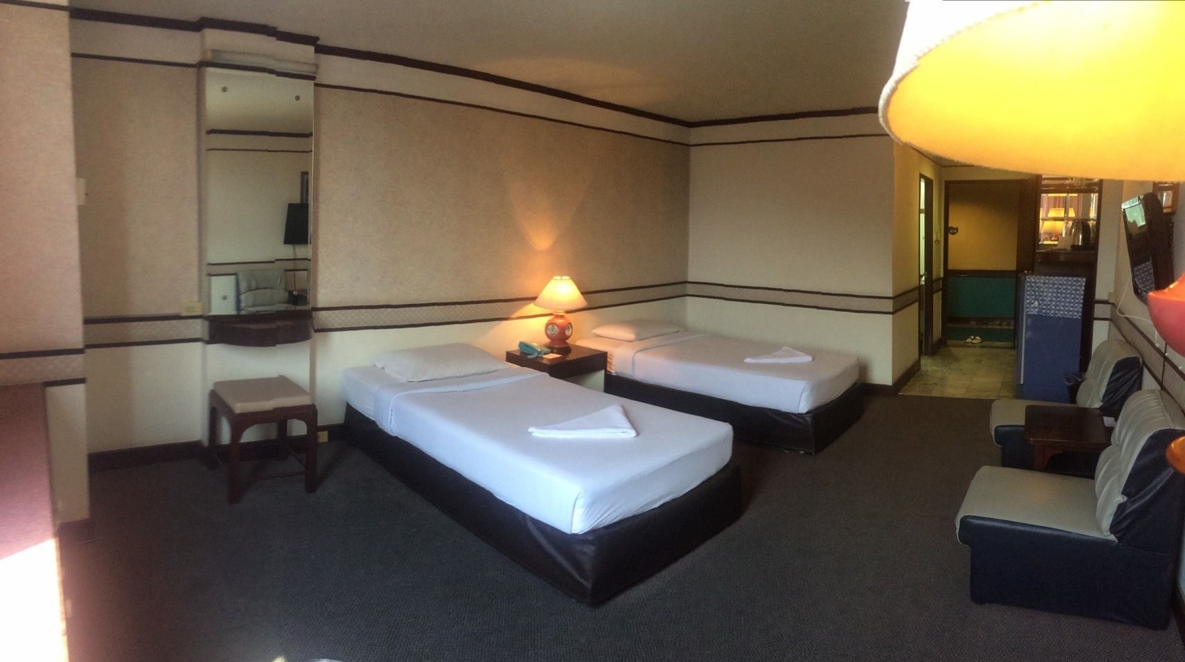 A hotel room with two beds, a desk, a chair, a lamp, and a sofa.