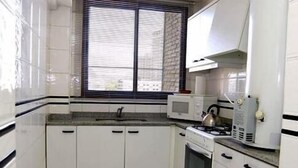 A compact kitchen with white cabinets, a microwave, a kettle, and a stove. - Complejo Recoleta (Mendoza)