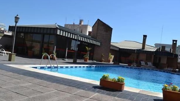 A rooftop pool with a clear blue sky, a modern building with large windows, and potted plants. - Complejo Recoleta (Mendoza)