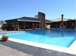 Una piscina con deck de baldosas, un espacio de descanso cubierto y plantas en macetas.
