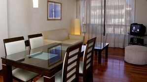 A dining area with a glass-top table, wooden chairs, a sofa, and a TV on a stand. - Complejo Recoleta (Mendoza)