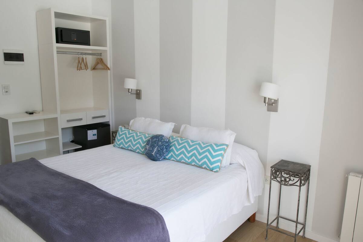 A bedroom with a bed, a wardrobe, a bedside table, and a wall-mounted lamp.