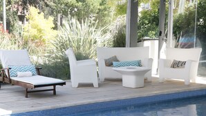 A poolside area with white lounge chairs and a small white table, surrounded by greenery. - Hotel Valeria (Valeria del Mar)