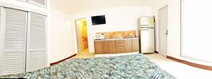 A bedroom with a bed, a wardrobe, a small kitchenette with a microwave, and a TV.