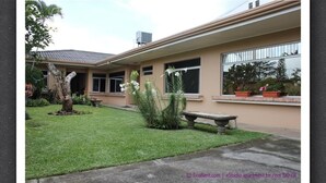 Un edificio residencial con césped cuidado, plantas en macetas y un banco.
