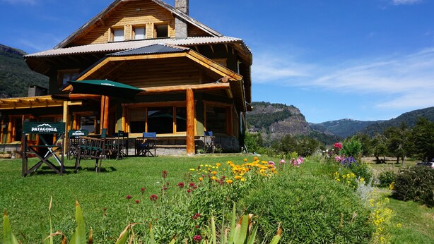 Una cabaña de madera con un patio, mobiliario exterior y vistas de las montañas circundantes.
