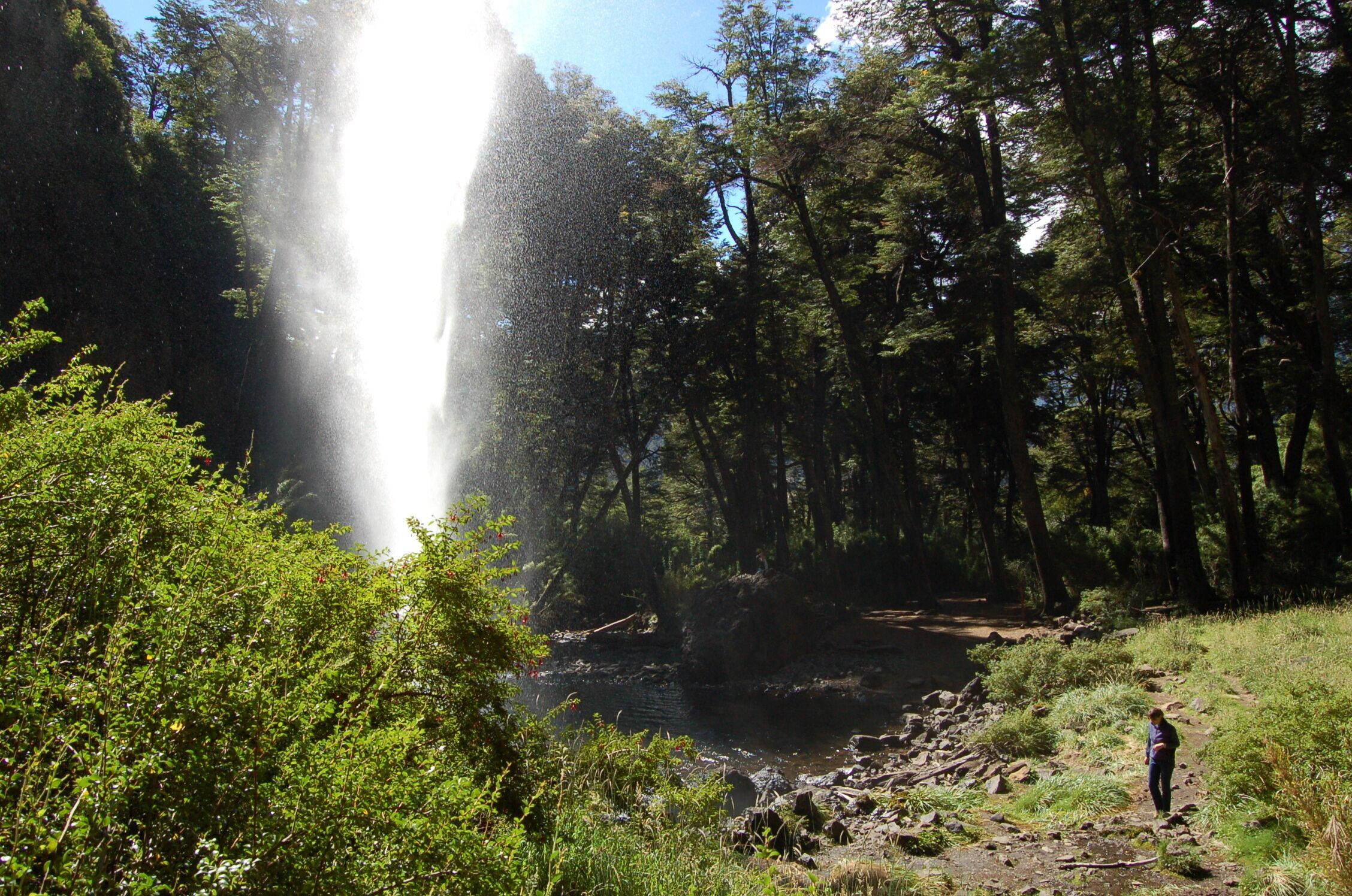A waterfall in a forested area with a person standing near the water.