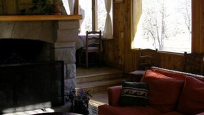 Una habitación acogedora con una chimenea de piedra, un sofá rojo y un ventanal con vistas a árboles.