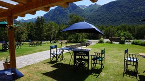 Un patio al aire libre con mesas y sillas, un paraguas azul y una vista de montañas al fondo.