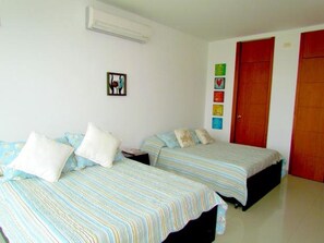 A room with two beds, a wall-mounted air conditioner, and a door with a red frame.