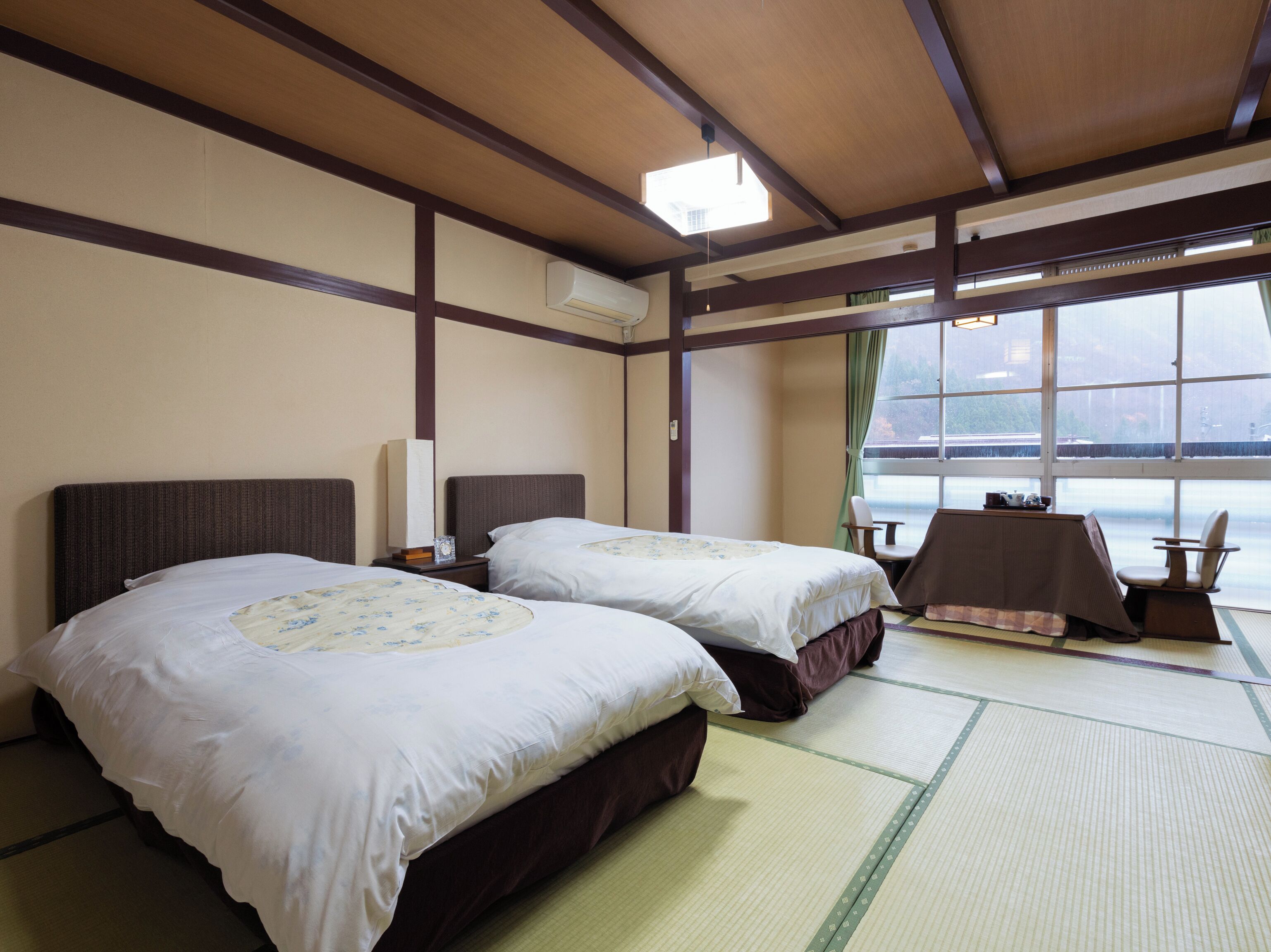 Quarto de hotel com duas camas, uma mesa, cadeiras, vista para o mar e piso de tatame.