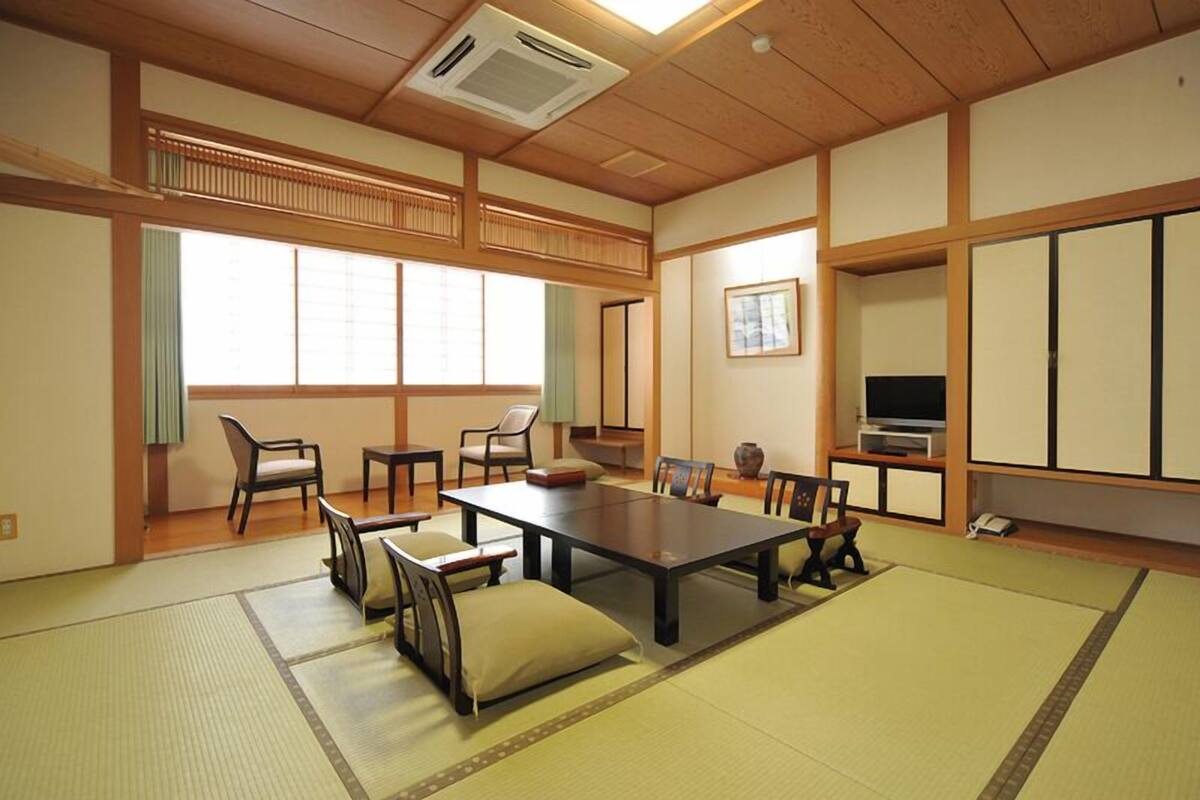 Ett traditionellt japanskt rum med tatamimattor på golvet, ett lågt bord, stolar, en TV och skjutdörrar.