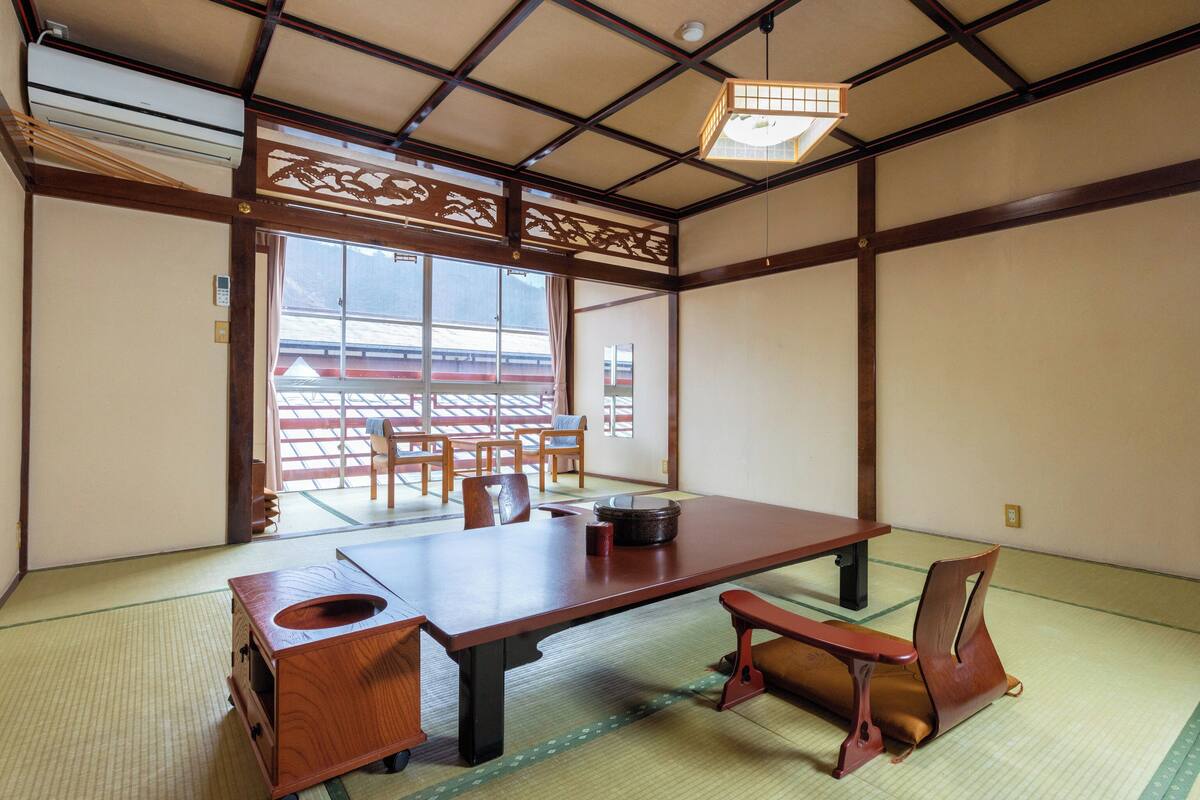 Ett traditionellt japanskt rum med tatamimattor på golvet, ett lågt bord, stolar och en skjutdörr som leder ut till en balkong.